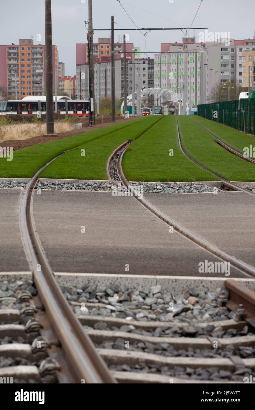 Die Schienen fahren auf der Straße vorbei, dann steinigen sie auf grünem Gras, das den Blick in Richtung Straßenbahnen in der Ferne lenkt. Stockfoto