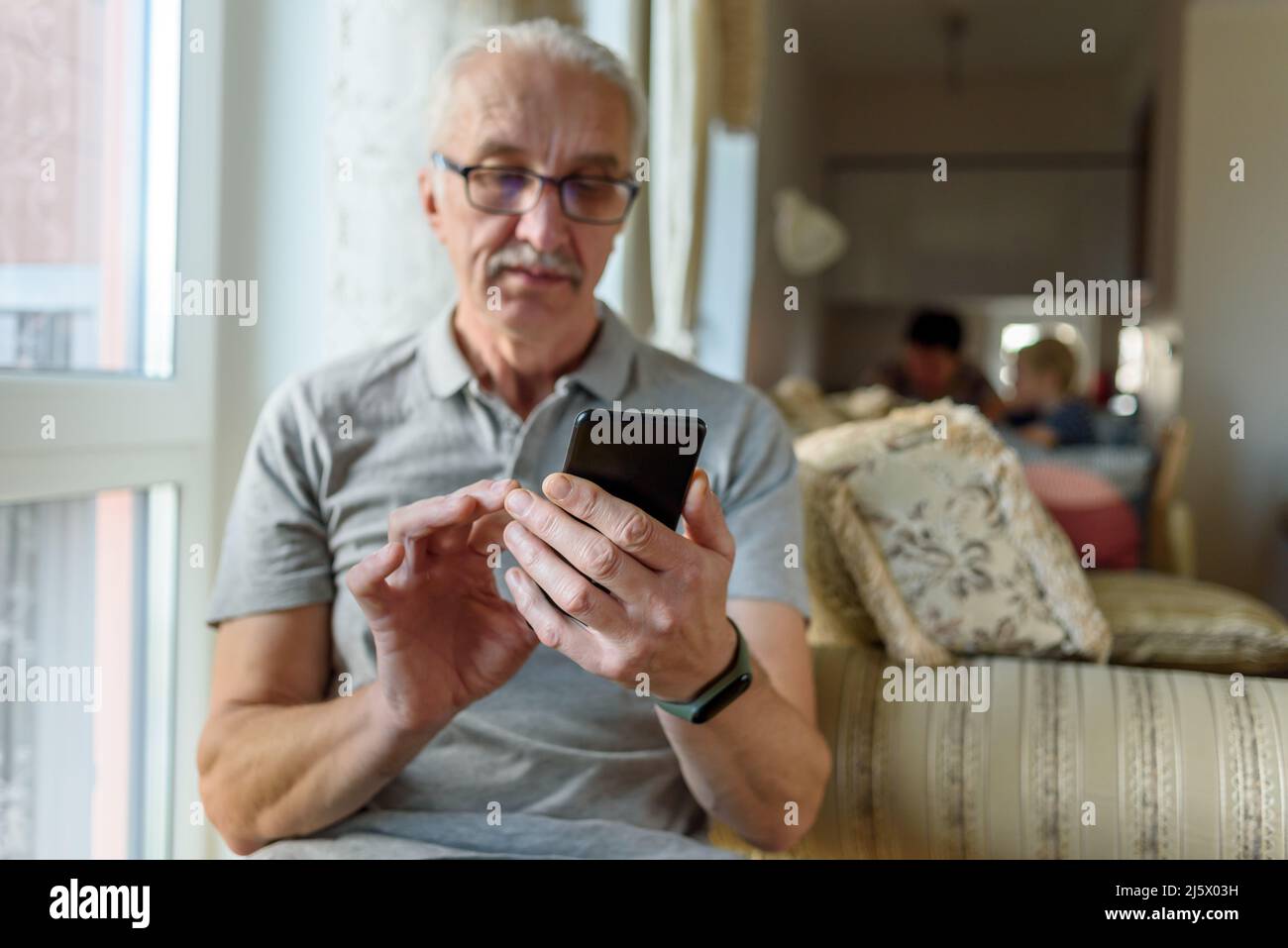 Älterer Mann in einer Brille, der zu Hause ein Mobiltelefon verwendet Stockfoto