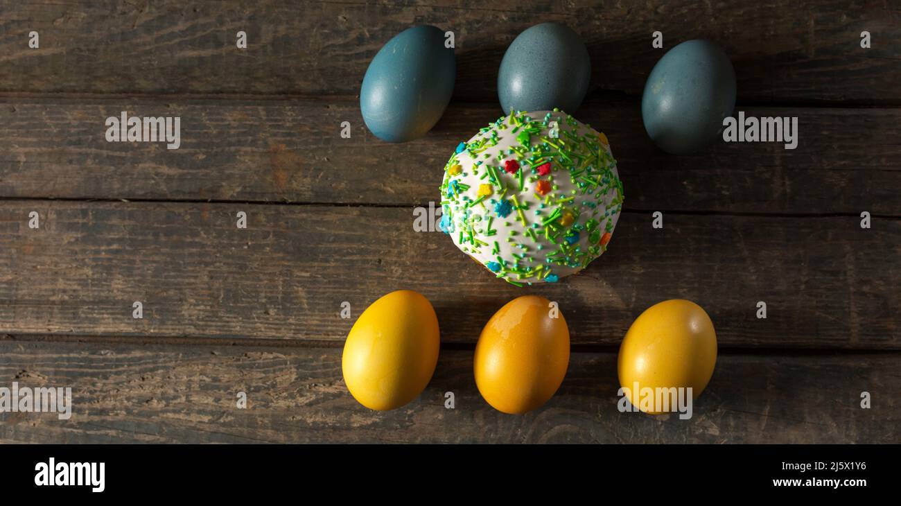 Bemalte Eier für Ostern in den Farben der Flagge der Ukraine und ein Osterkuchen in der Mitte. Gelb und blau (Cyan). Auf Holzstruktur. Konzept: Lebensmittel, Stockfoto