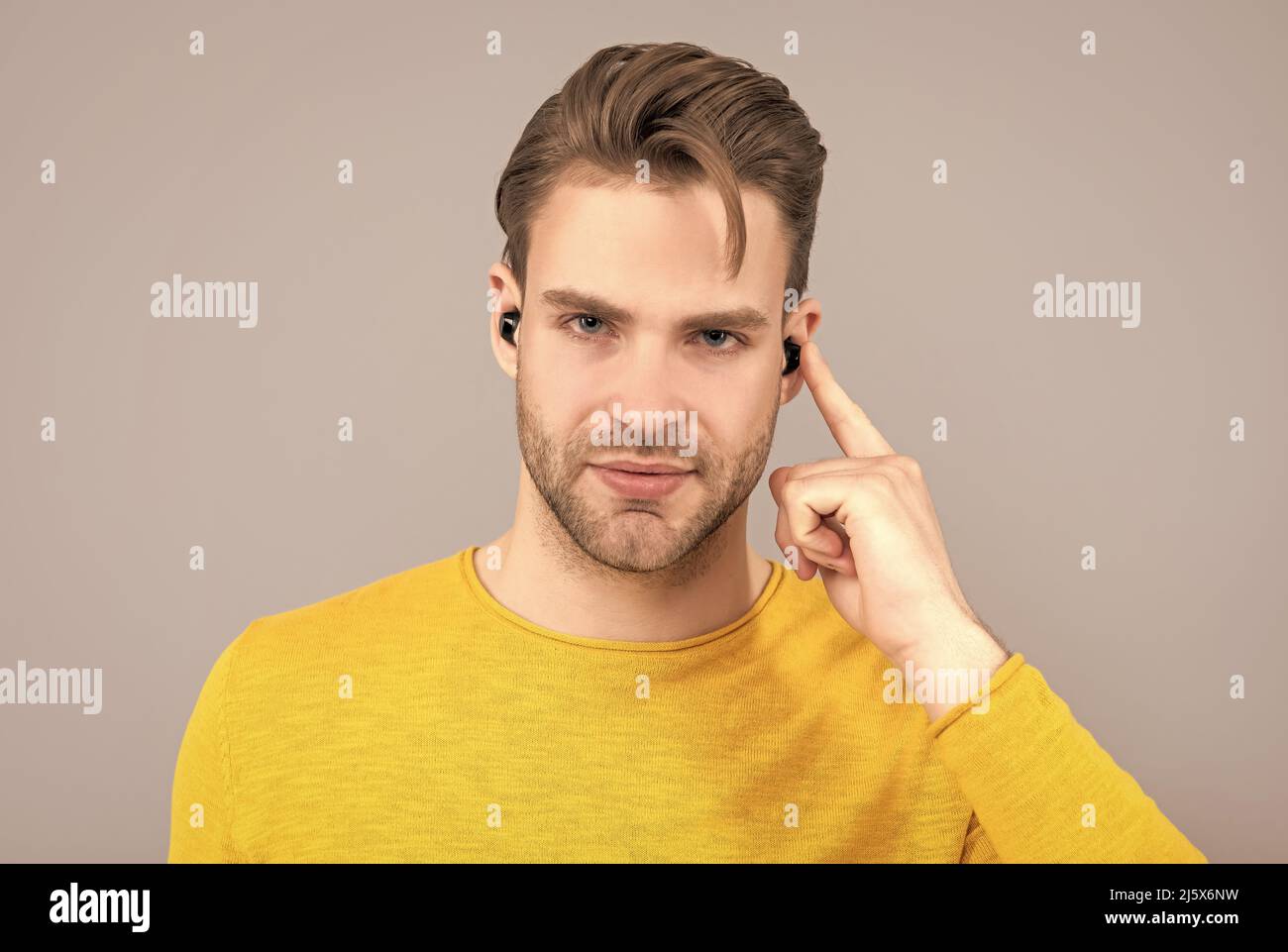 Schöner Kerl zeigen Finger auf Ohrhörer Kopfhörer im Ohr grauen Hintergrund, hören Stockfoto