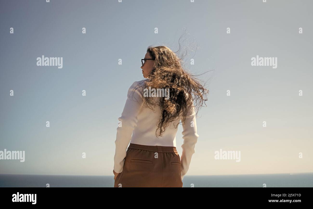 Ihr Haar fließt im Wind. Frau mit langen Haaren steht auf See. Stilvolle Mädchen mit welligen Frisur Stockfoto