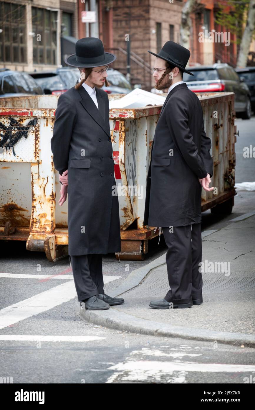 Zwei orthodoxe jüdische junge Männer mit ähnlichen Posen und ähnlichen Kleidern unterhalten sich auf der Lee Avenue in williamsburg, Brooklyn, New York City. Stockfoto