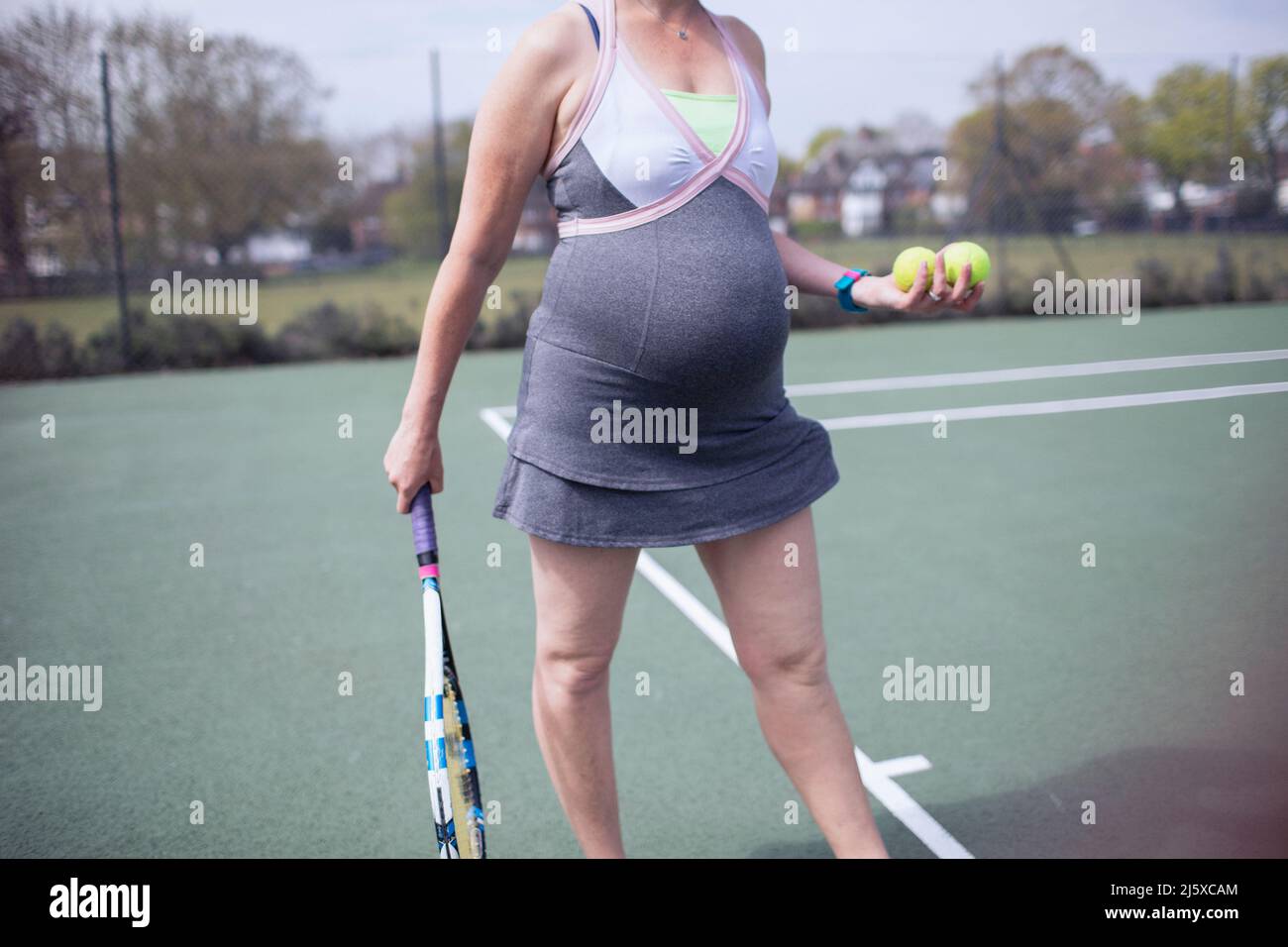 Eine Schwangerin im Kleid, die Tennis auf dem Tennisplatz spielt Stockfoto