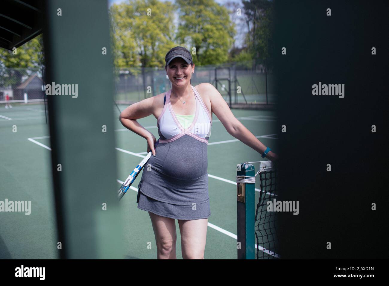 Porträt zuversichtlich, schwanger Frau in Kleid auf sonnigen Tennisplatz Stockfoto
