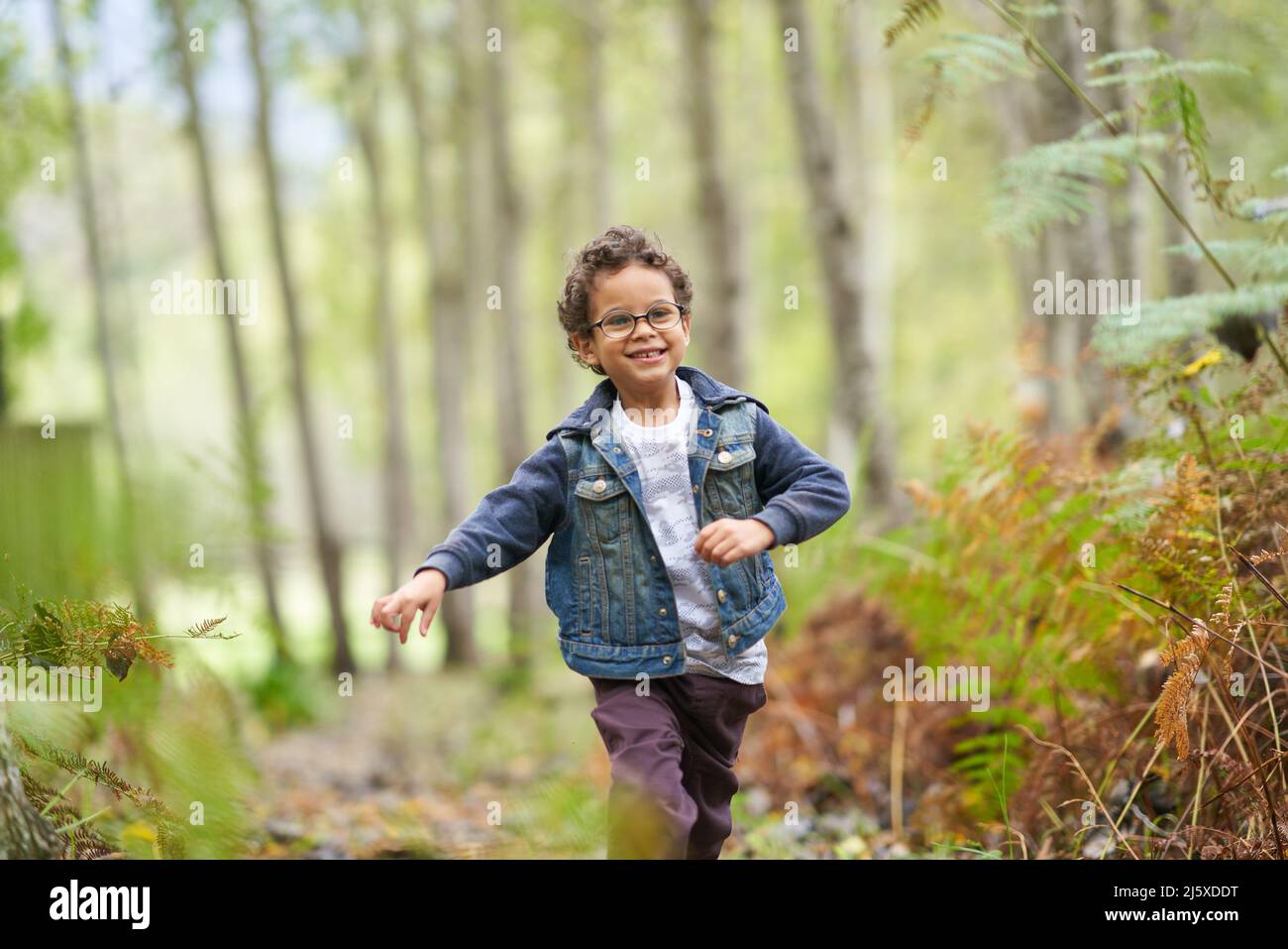 Portrait glücklicher Junge, der im Wald läuft Stockfoto