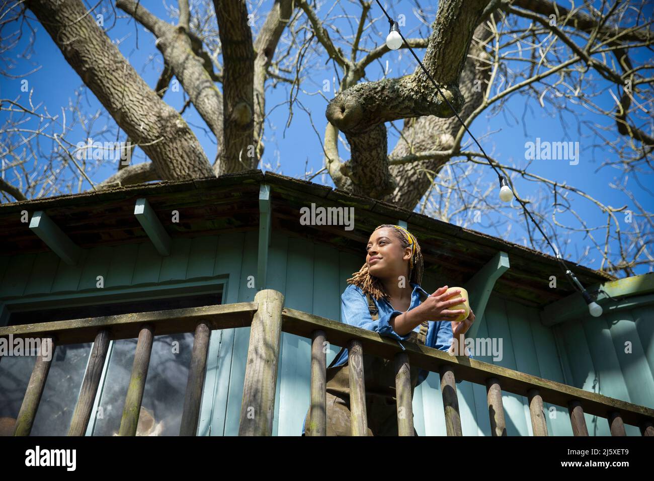 Lächelnde junge Frau, die Kaffee auf dem Balkon des Baumhauses trinkt Stockfoto