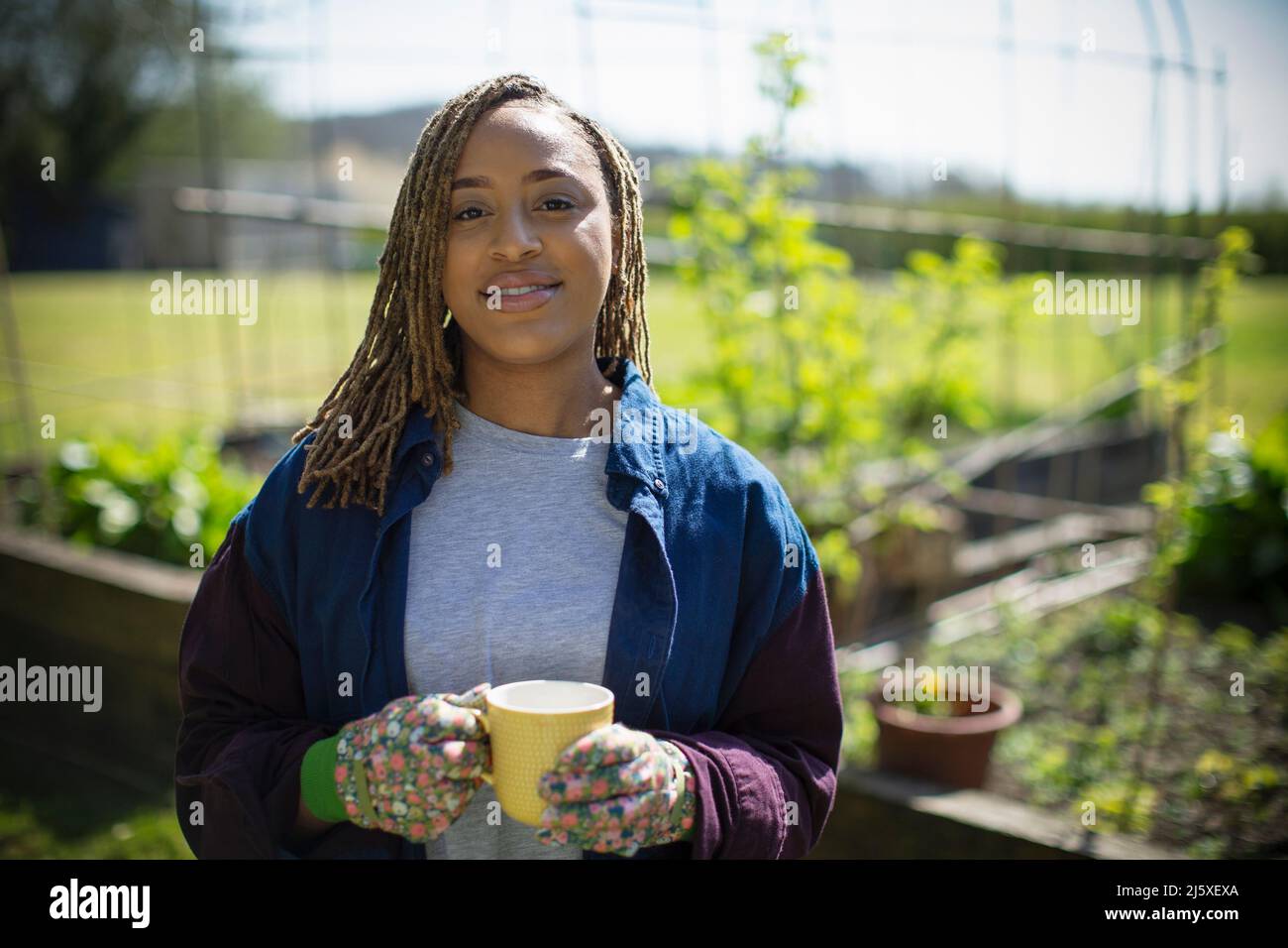 Porträt lächelnde junge Frau, die im sonnigen Garten Tee trinkt Stockfoto