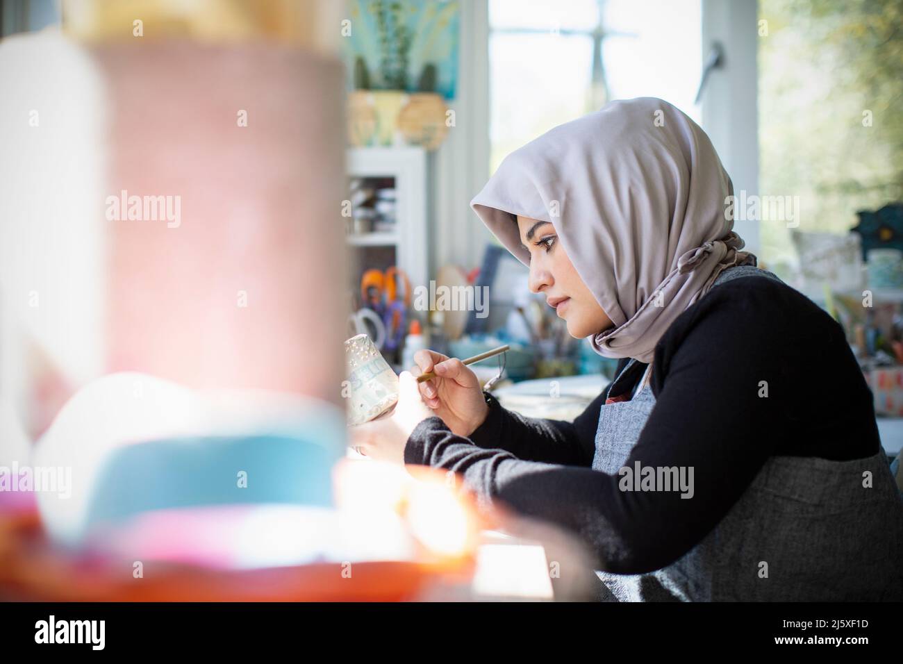 Fokussierte junge Künstlerin in Hijab Malerei Keramik im Kunststudio Stockfoto