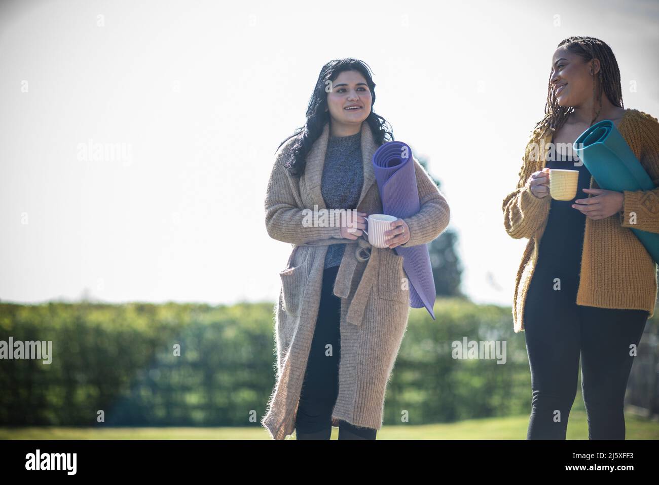 Junge Frauen befreundet sich mit Kaffee und Yogamatten draußen Stockfoto