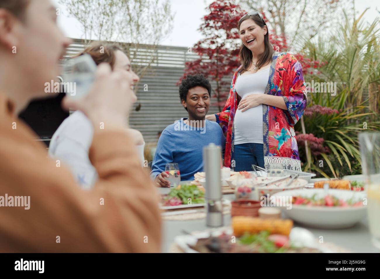 Glückliches, trächtiges Paar, das mit Freunden auf der Terrasse zu Mittag essen kann Stockfoto
