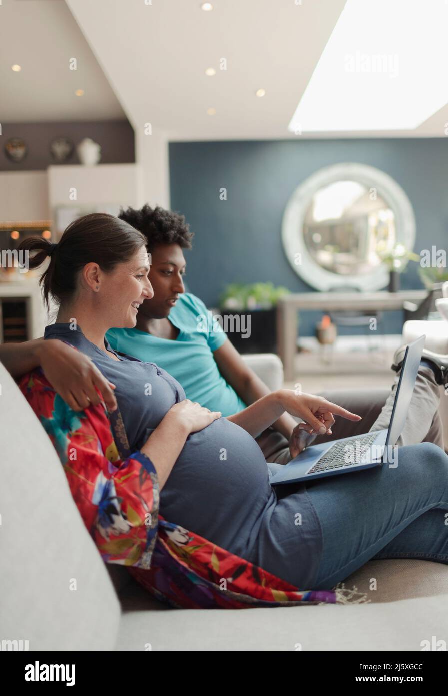 Schwanger Paar mit Laptop auf Wohnzimmer Sofa Stockfoto