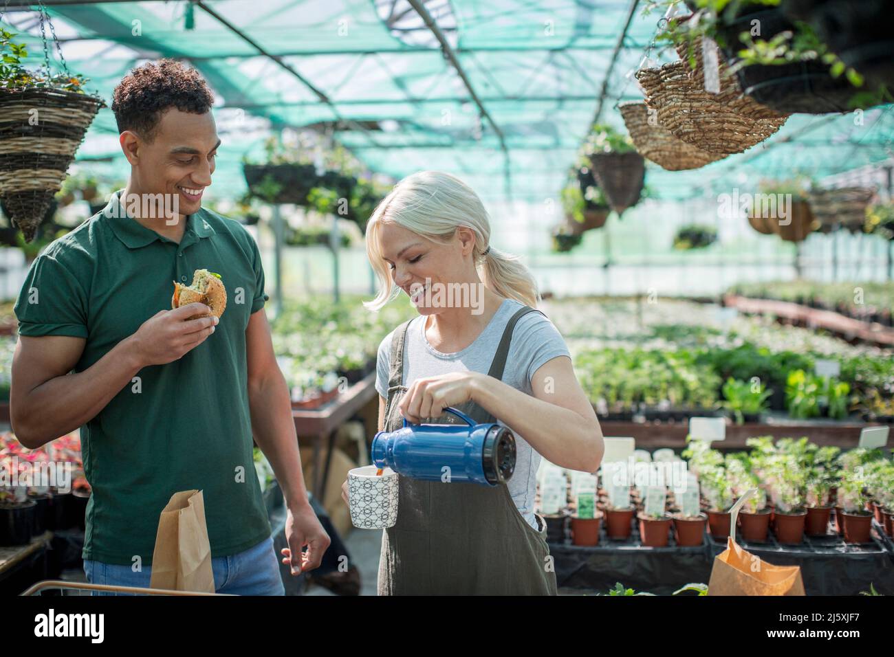 Besitzer von Pflanzenzügnereien genießen Tee und Mittagessen im sonnigen Gewächshaus Stockfoto