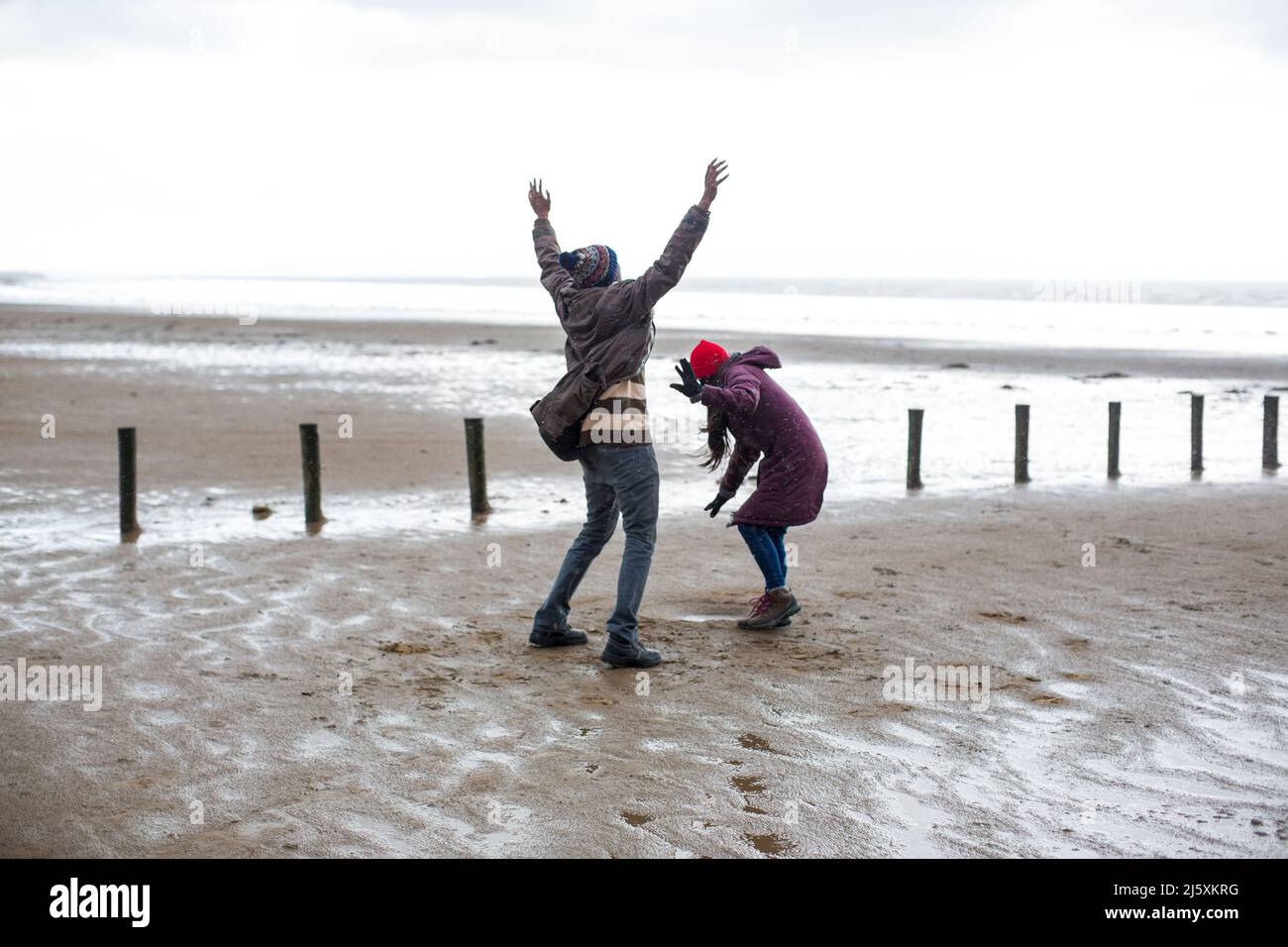 Glückliches verspieltes Paar am nassen Winterstrand Stockfoto