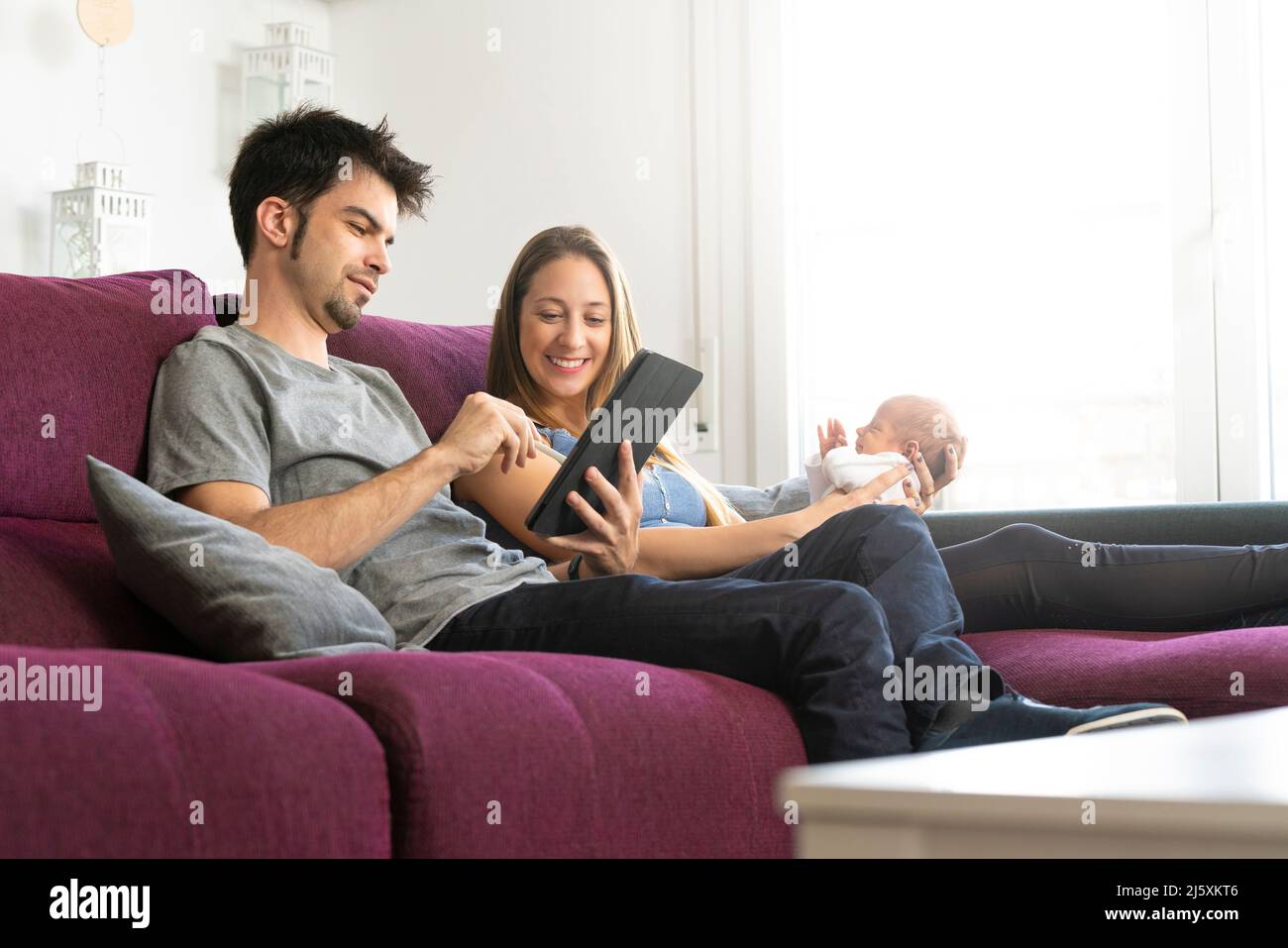 Mutter und Vater mit ihrem Neugeborenen auf dem Sofa mit einem digitalen Tablet Stockfoto