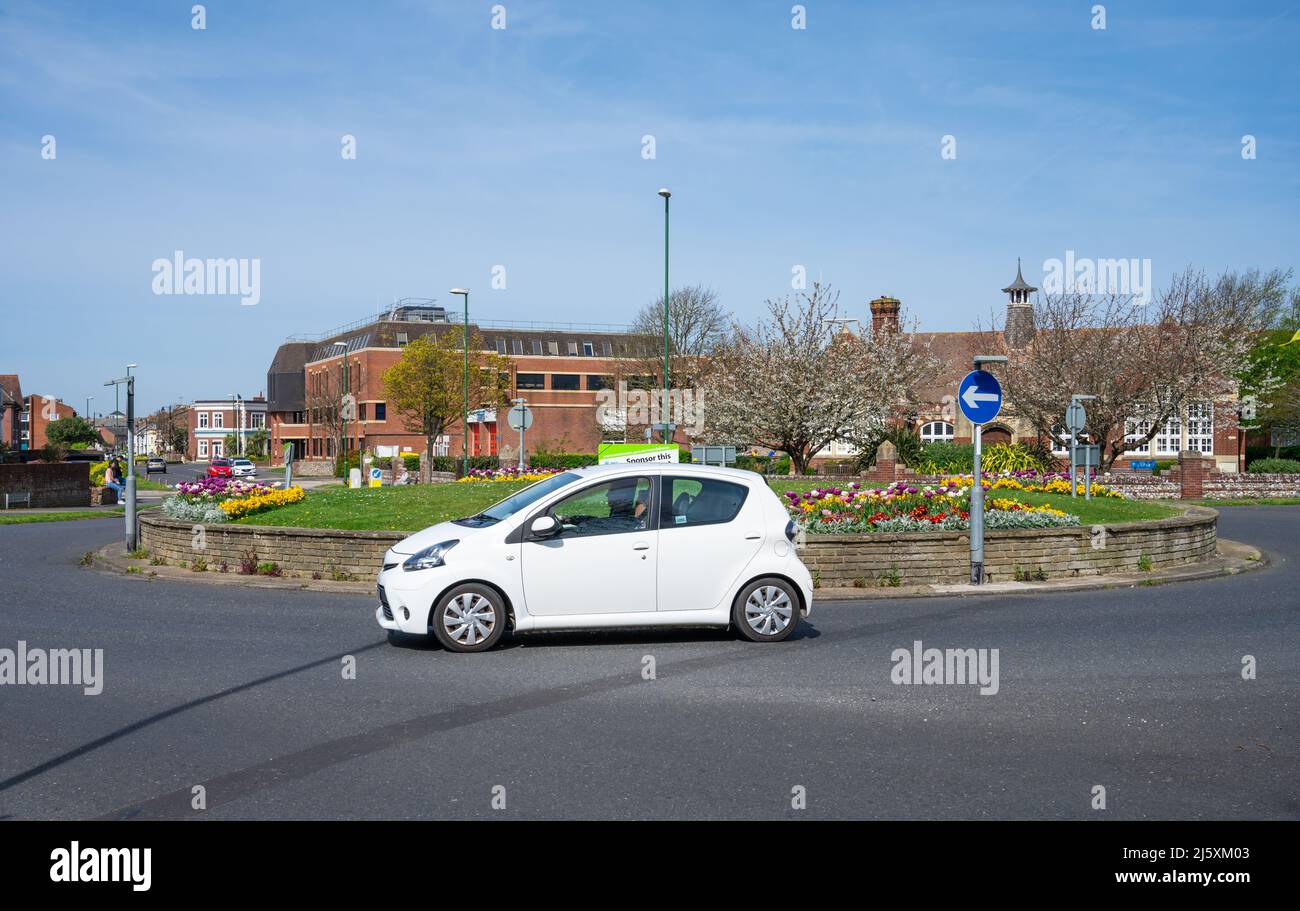 Auto, das an einem kleinen von Großbritannien gesponserten Kreisverkehr auf einer Straße in England, Großbritannien, herumfährt. Stockfoto