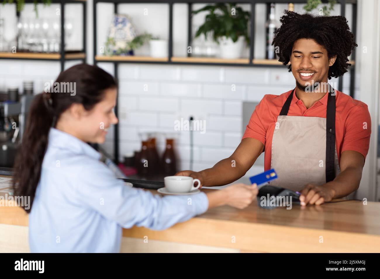 Happy Millennial african american Curly männlichen Kellner im Vorfeld gibt frischen Kaffee an Kunden Stockfoto