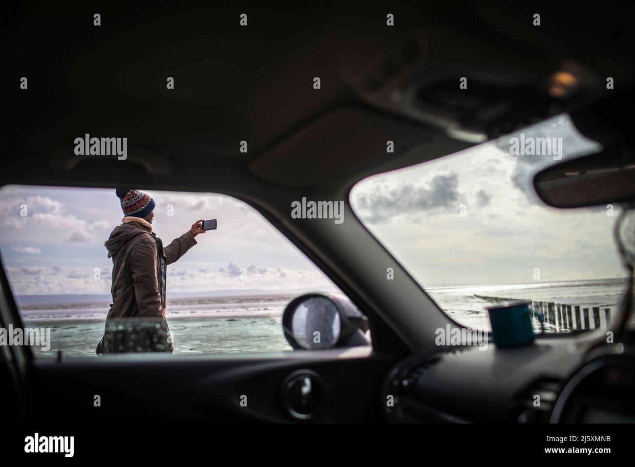 Mann mit Kameratelefon am Winterstrand vor dem Auto Stockfoto
