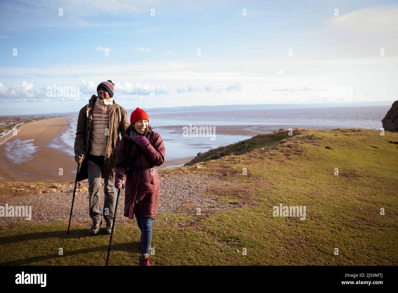 Wanderpaar auf einer sonnigen Klippe über dem winterlichen Meeresstrand Stockfoto Wanderpaar auf einer sonnigen Klippe über dem winterlichen Meeresstrand Stockfoto