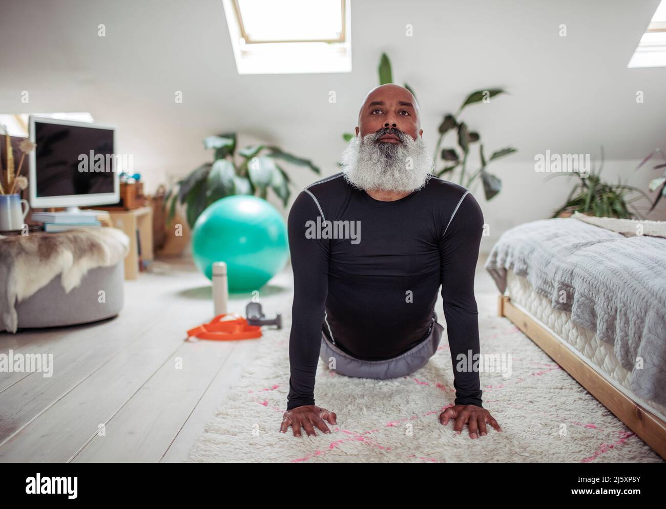 Reifer Mann mit Bart, der zu Hause Yoga nach oben hin praktiziert Stockfoto