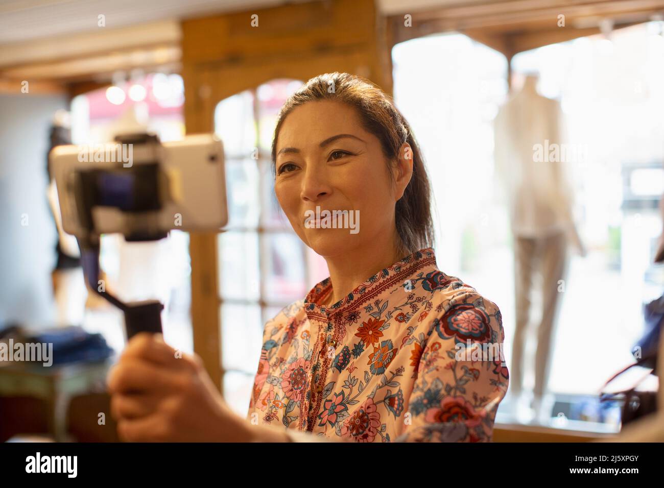 Weibliche Ladenbesitzerin vloggt mit Smartphone in der Boutique Stockfoto