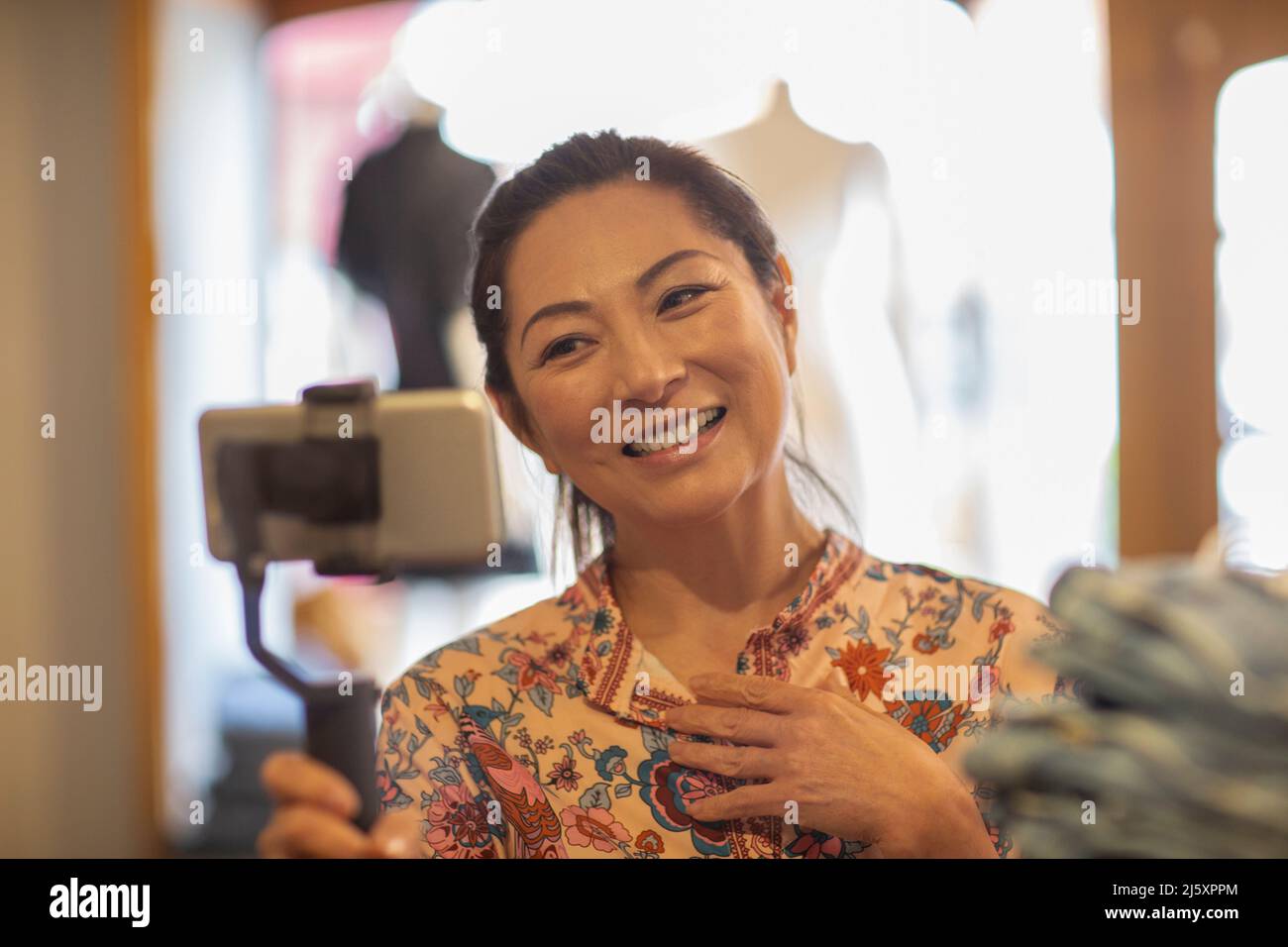 Lächelnde weibliche Ladenbesitzerin vloggt mit Smartphone und Selfie-Stick Stockfoto