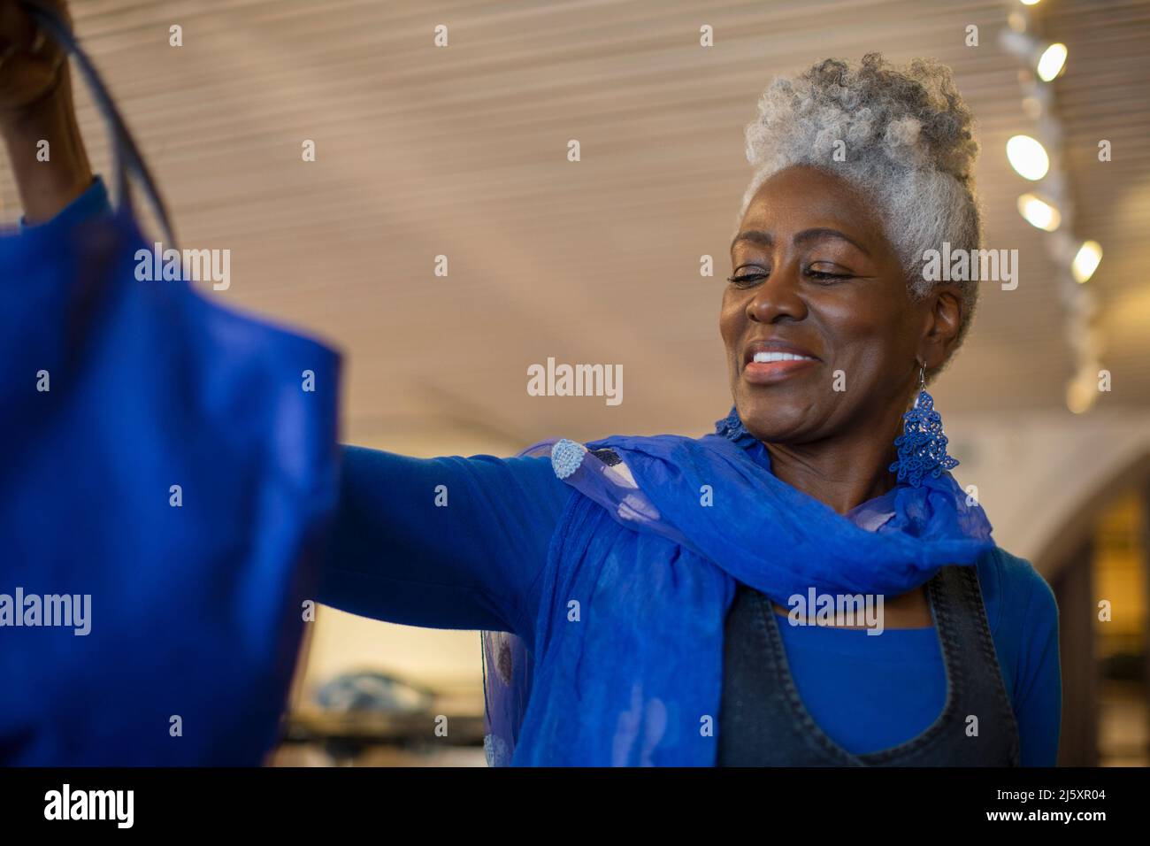 Glückliche ältere Frau im blauen Einkaufen Stockfoto