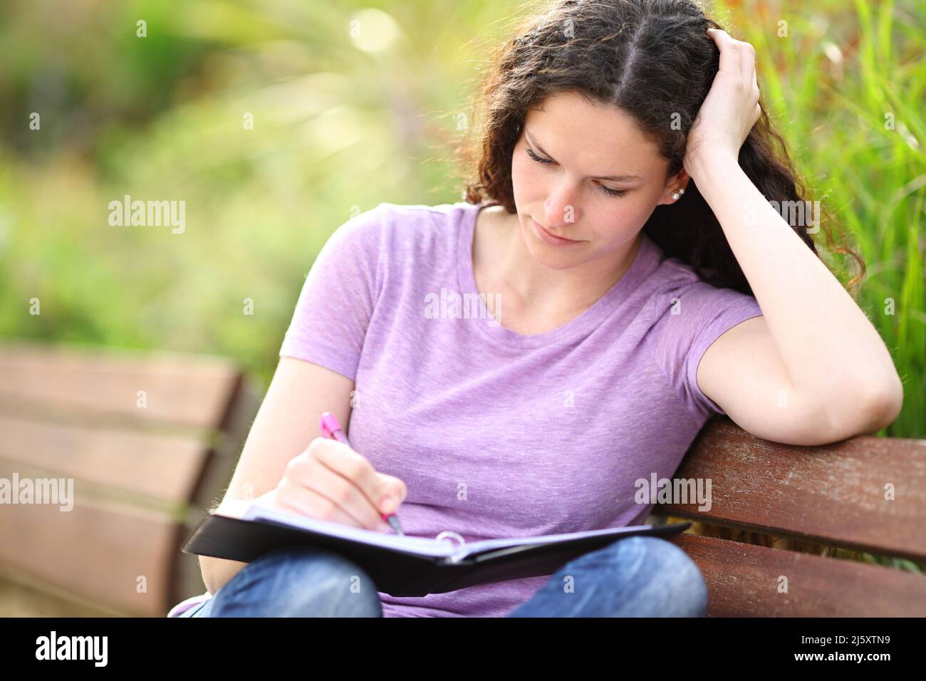 Geballte Frau, die auf einem Notizbuch auf einer Bank in einem Park sitzt Stockfoto