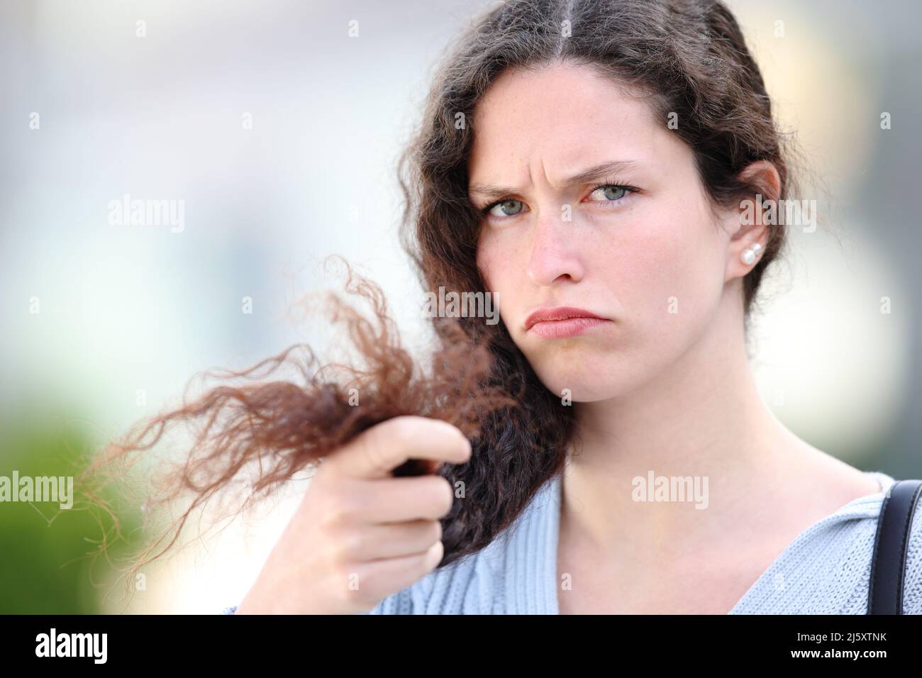 Verärgerte Frau mit lockigen Haaren, die sich über gespaltene Enden auf der Straße beschwert Stockfoto
