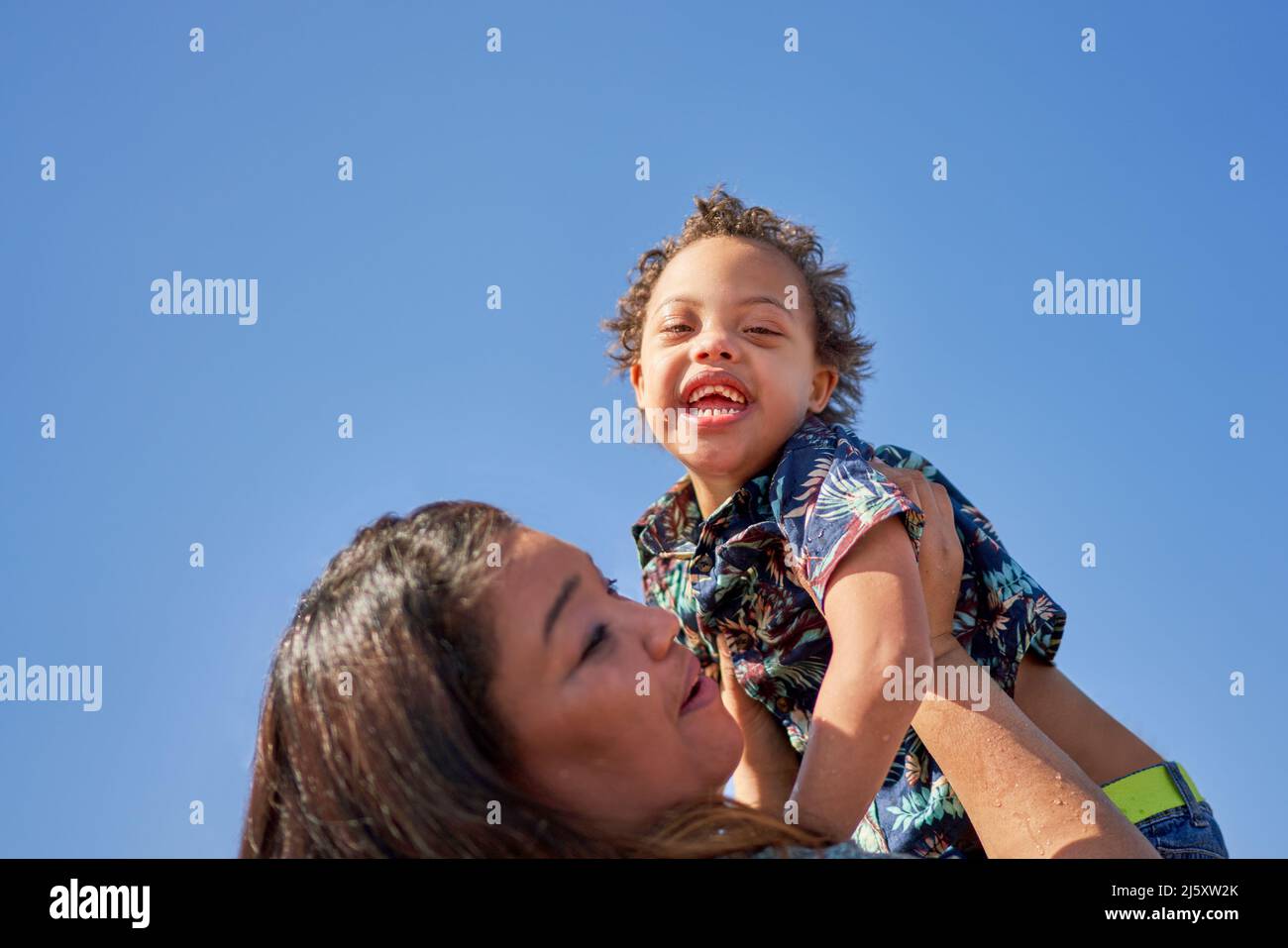 Portrait Mutter hebt glücklichen, sorglosen Sohn mit Down-Syndrom Stockfoto