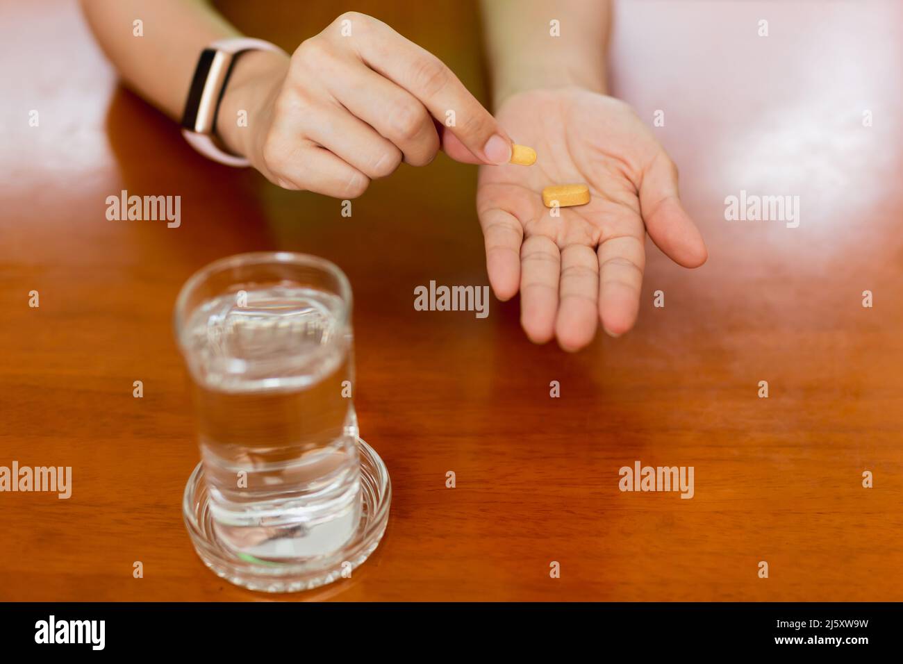 Frau hält Vitamin-C-Pillen mit einem Glas Wasser auf dem Tisch. Stockfoto