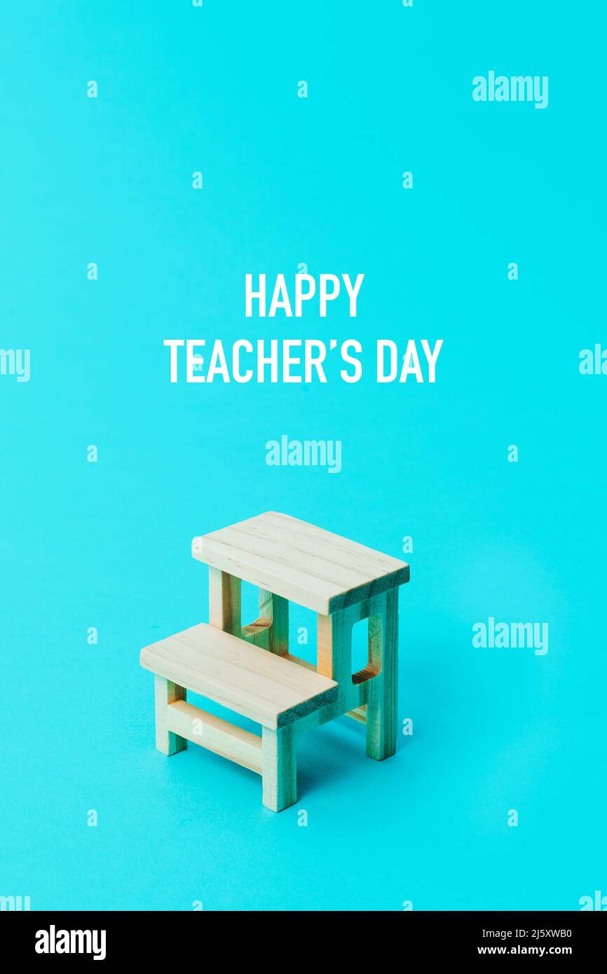 Der Text Happy Teachers Day und ein hölzerner Schultisch auf blauem Hintergrund Stockfoto