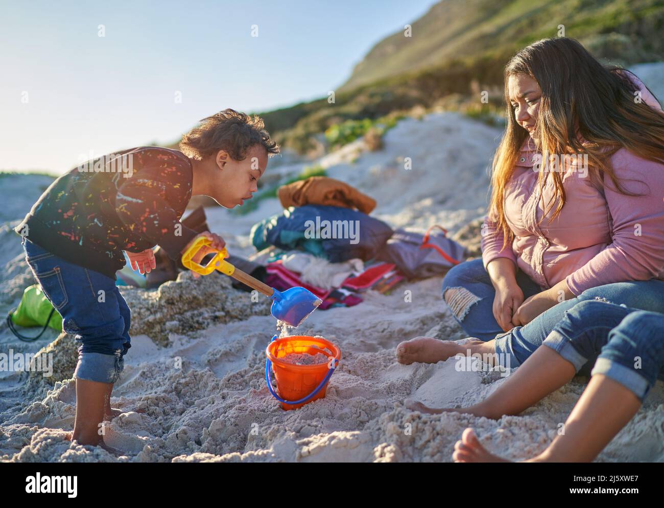 Netter Junge, der am Strand mit Schaufel und Eimer im Sand spielt Stockfoto