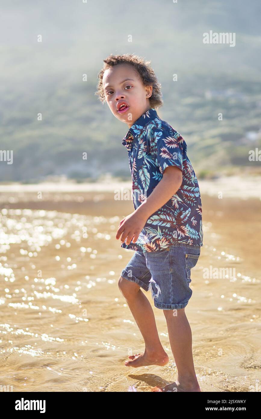 Portrait Junge mit Down-Syndrom waten im Meer am sonnigen Strand Stockfoto