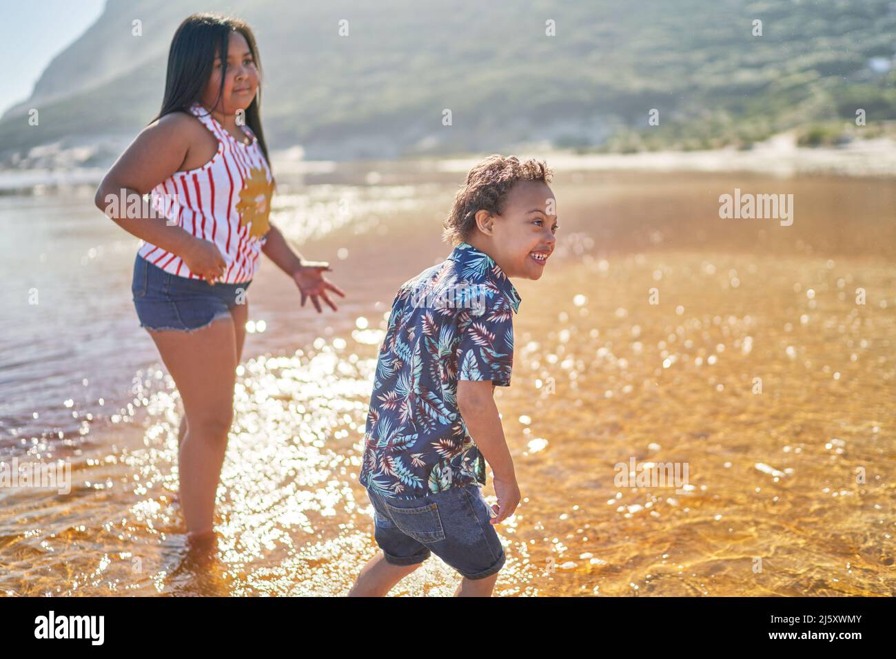 Fröhlicher Bruder und Schwester spielen in sonniger Meeresbrandung Stockfoto
