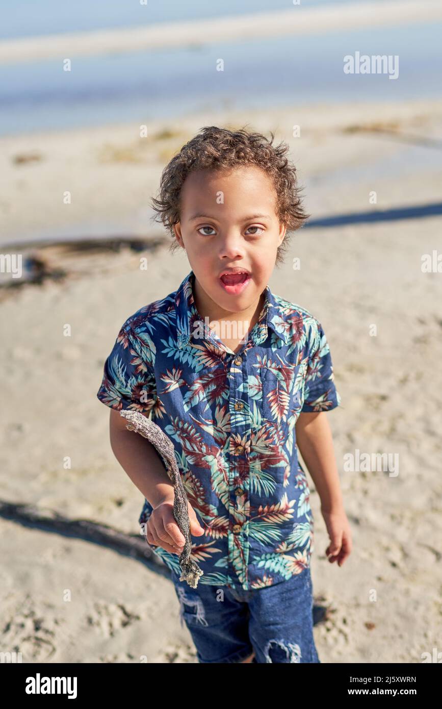 Porträt niedlichen Jungen mit Down-Syndrom halten Stock am Strand Stockfoto