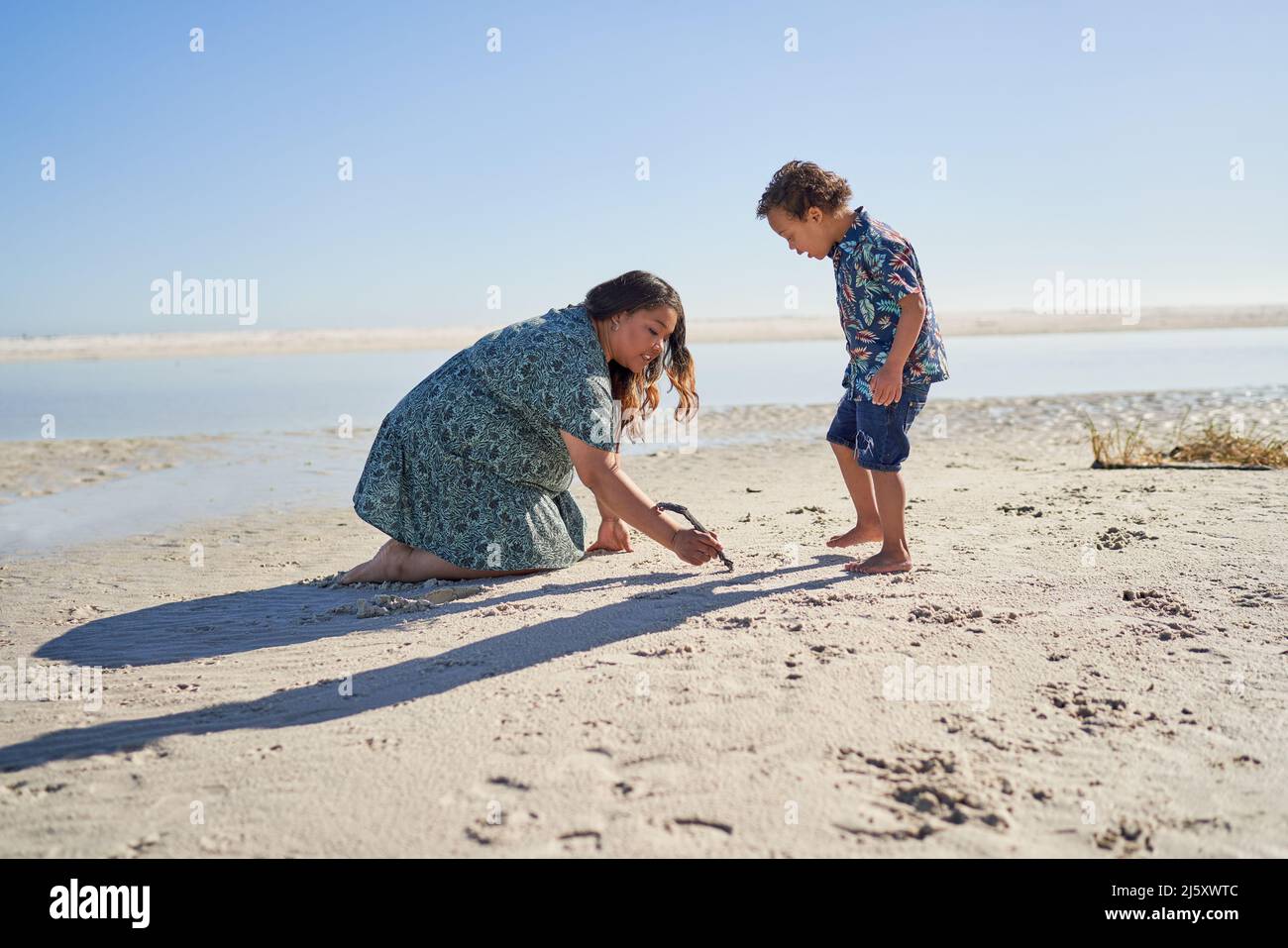 Mutter und Sohn mit Down-Syndrom ziehen im Sand mit Stock am Strand Stockfoto