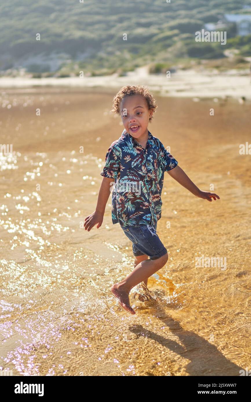 Sorgloser Junge mit Down-Syndrom, der im Ozean spritzt Stockfoto