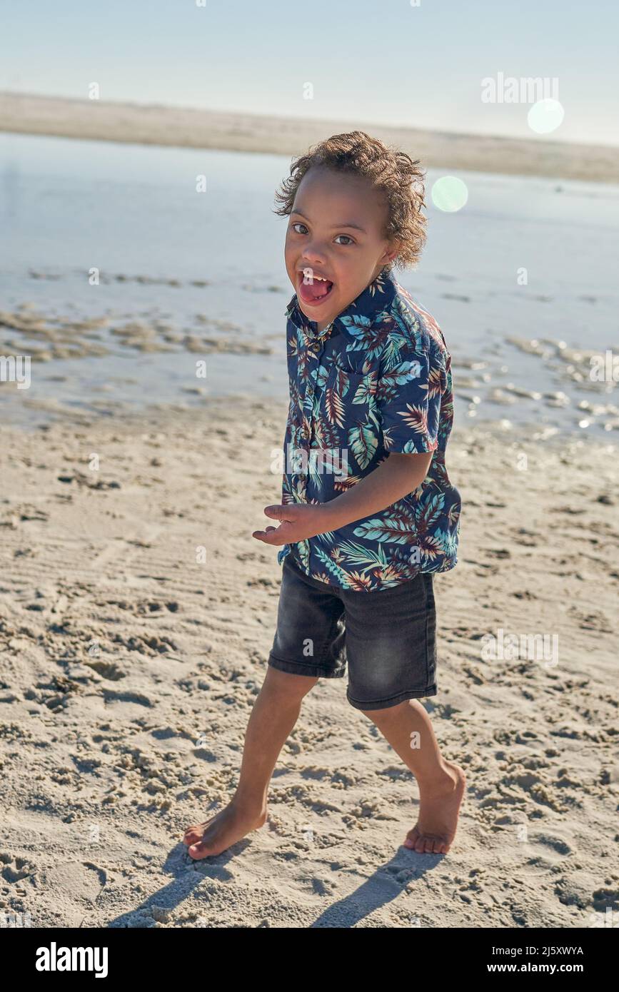 Portrait glücklicher Junge mit Down-Syndrom am sonnigen Strand Stockfoto