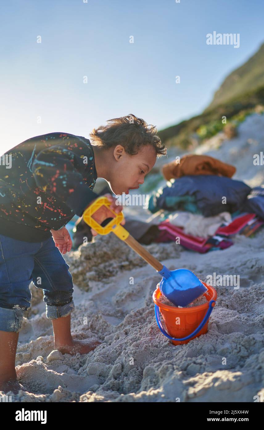 Junge mit Down-Syndrom spielt im Sand mit Schaufel und Eimer Stockfoto