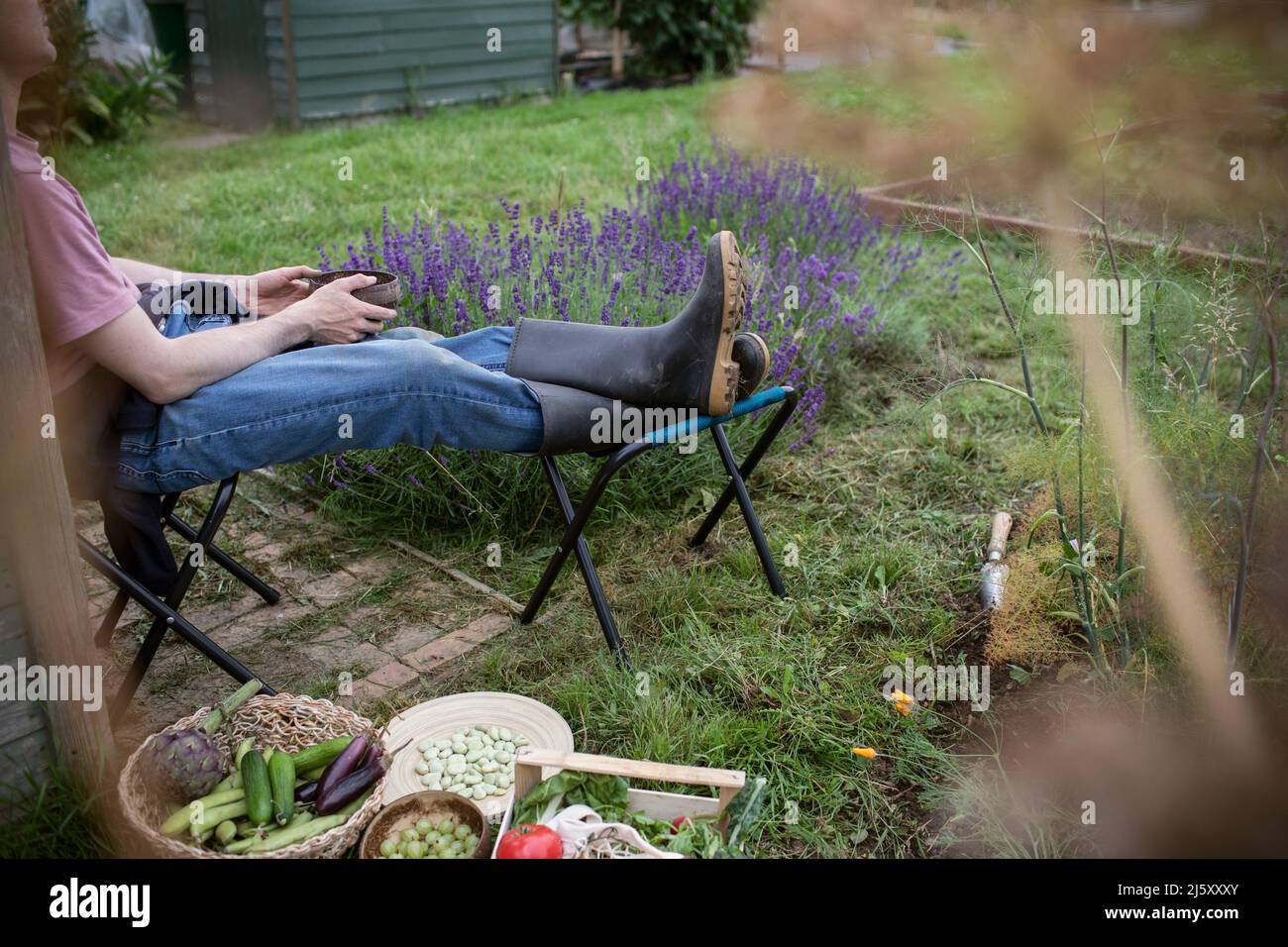 Mann, der sich im Garten mit geerntetem Gemüse entspannt Stockfoto