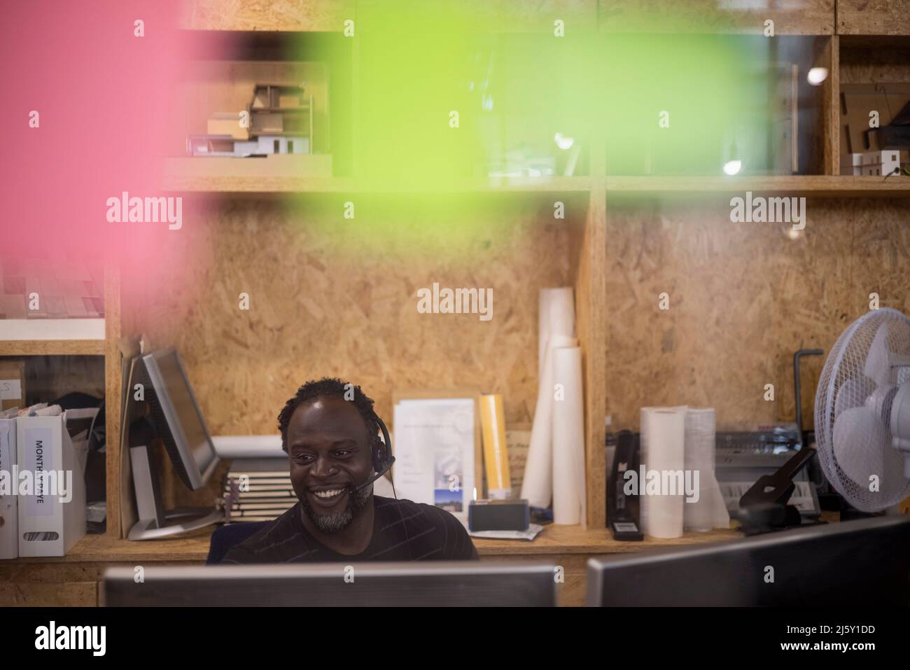 Lächelnder Geschäftsmann im Headset, der am Bürocomputer arbeitet Stockfoto