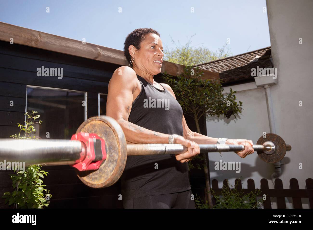 Starke reife Frau Gewichtheben mit Langhantel im Hinterhof Stockfoto