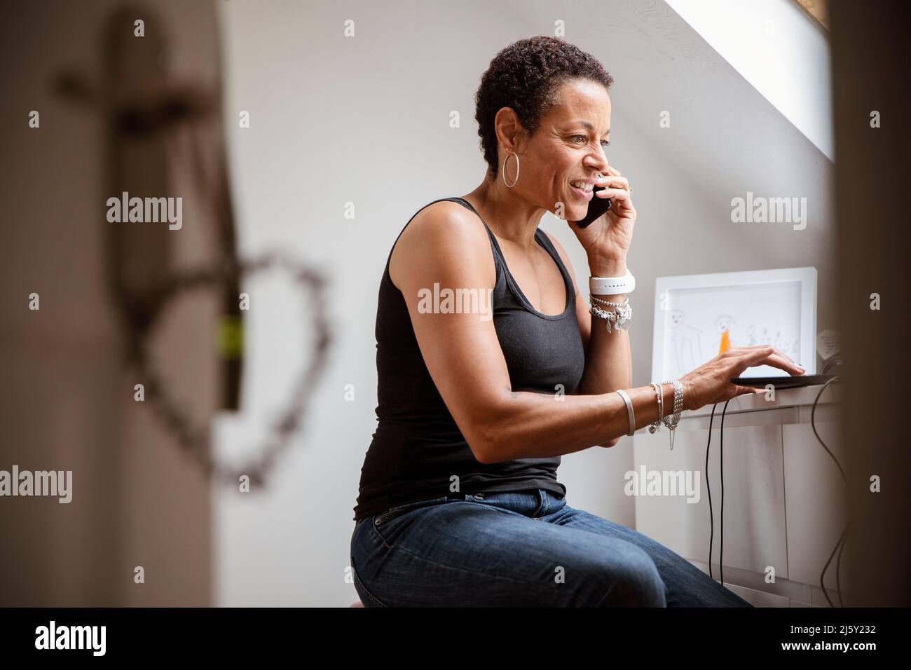 Reife Frau, die im Heimbüro auf dem Smartphone spricht Stockfoto