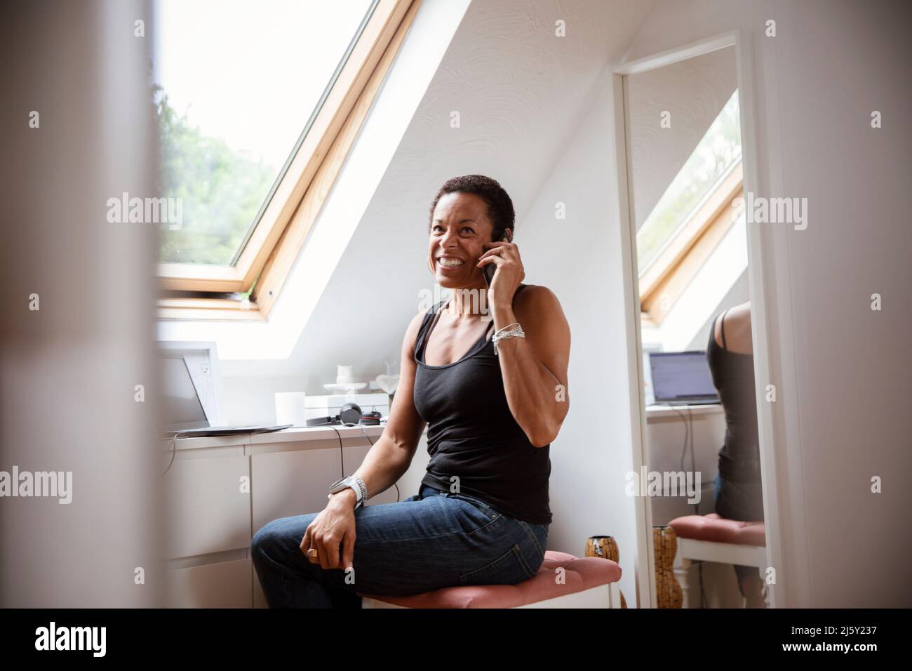 Lächelnde reife Frau, die zu Hause auf dem Smartphone spricht Stockfoto
