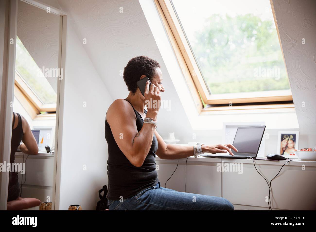 Frau, die von zu Hause aus am Laptop arbeitet und auf dem Smartphone spricht Stockfoto