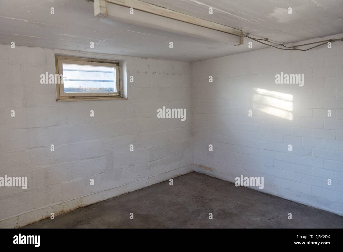 Ecke in einem leeren Kellerraum mit einem Fenster im Keller und einer Neonlampe Stockfoto
