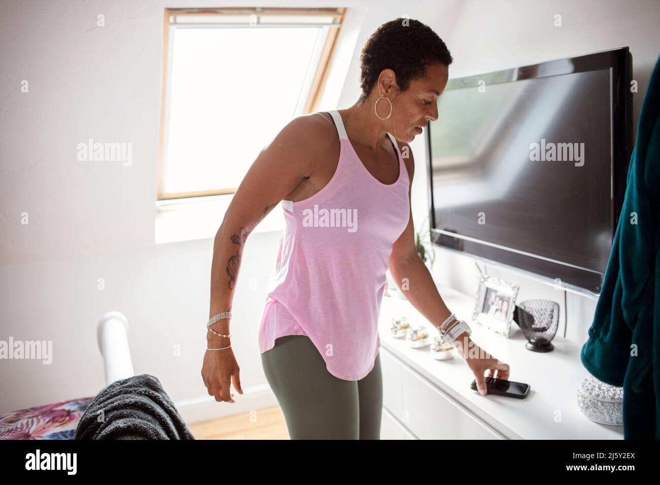 Athletische Frau, die im Schlafzimmer nach einem Smartphone greift Stockfoto