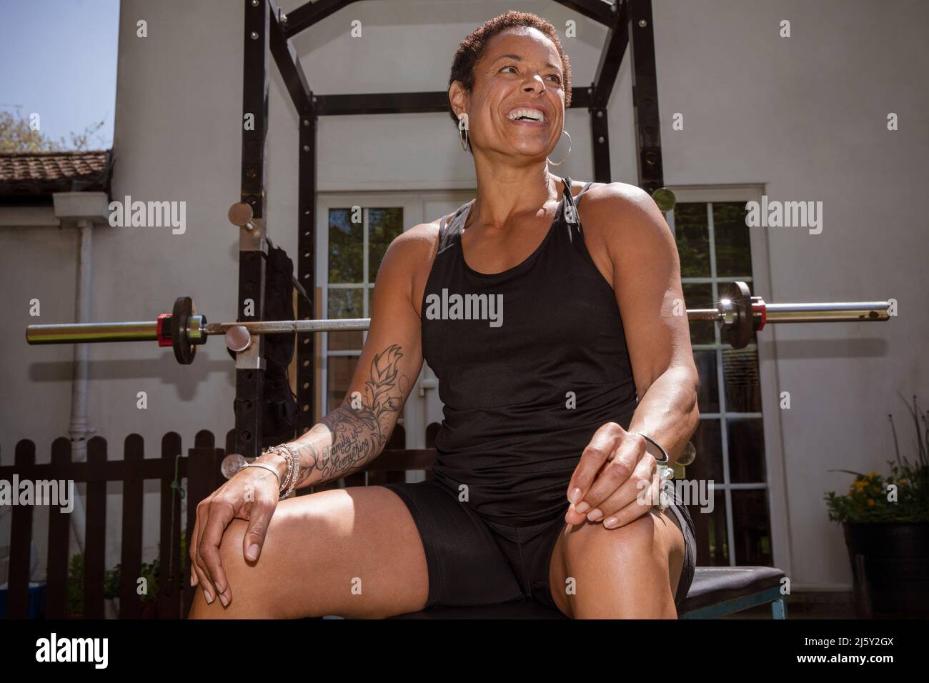 Portrait glückliche, selbstbewusste Frau Gewichtheben im sonnigen Hinterhof Stockfoto