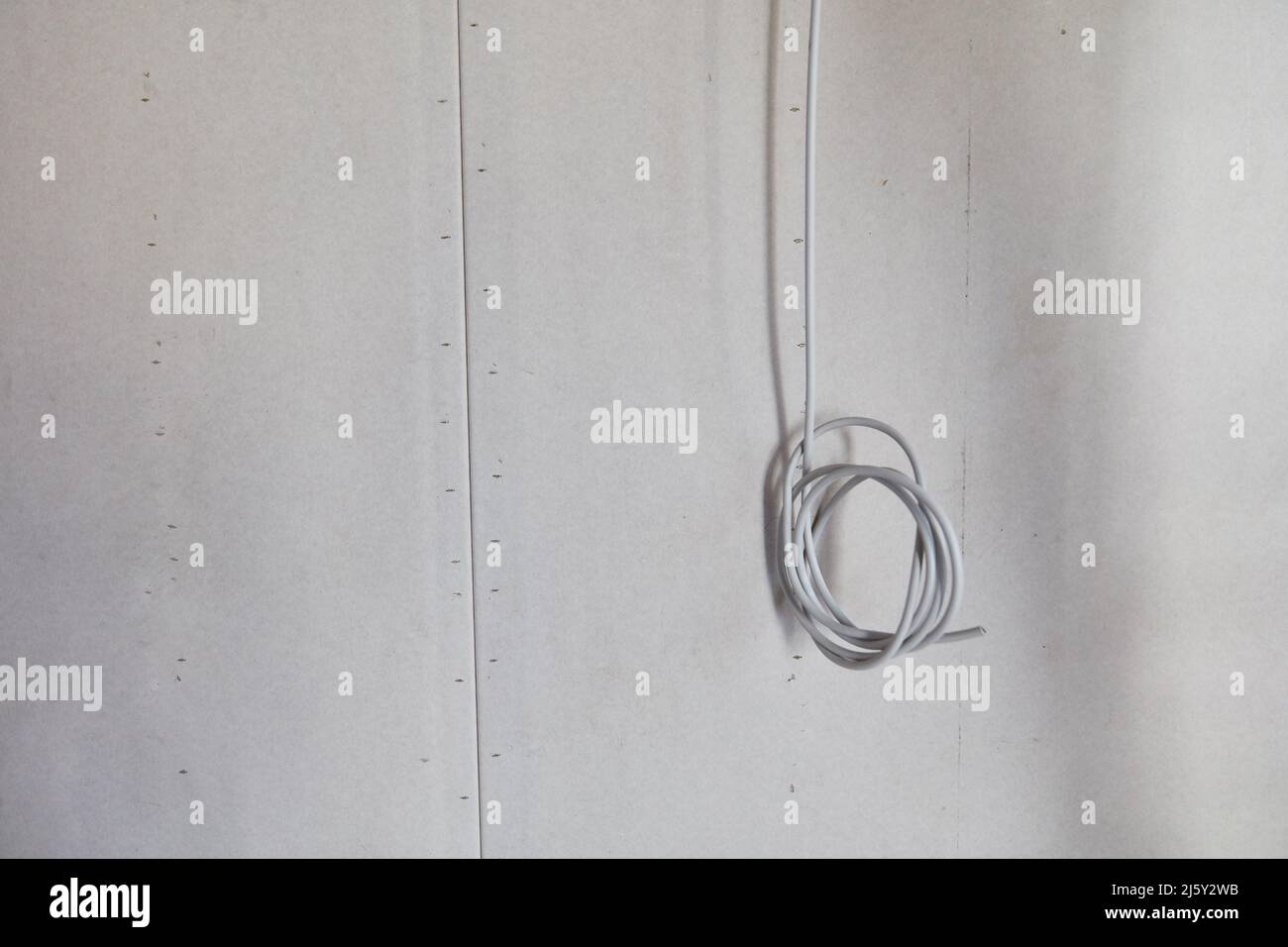 Graues gewalztes Kabel hängt von der Decke für die Elektroinstallation in Neubauten Stockfoto