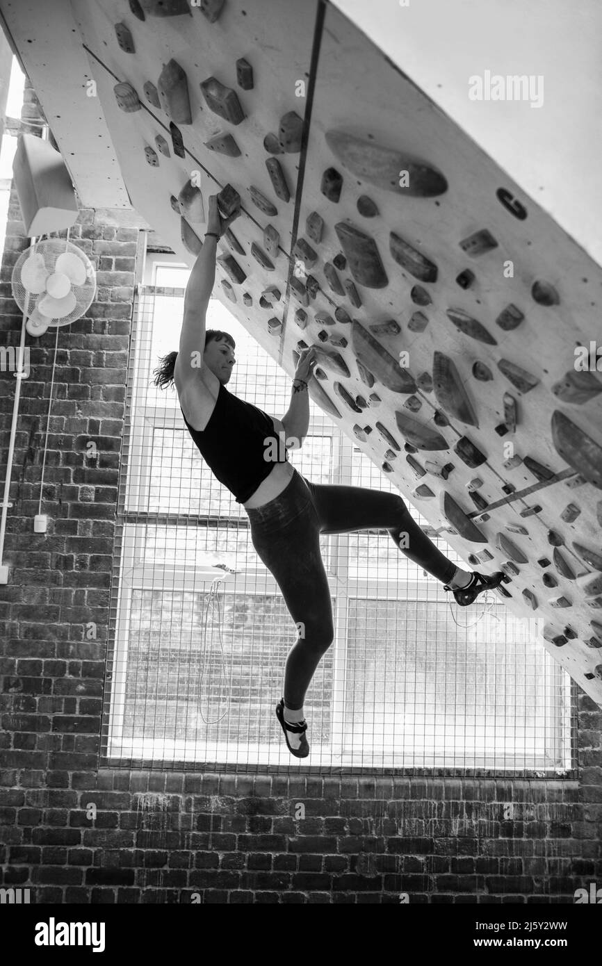 Junge Frau, die an einer Kletterwand hängt Stockfoto